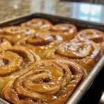 ['Close-up view of fluffy apple cinnamon rolls topped with creamy frosting.', 'Side view of freshly baked apple cinnamon rolls with visible apple chunks and cinnamon.', 'Juicy apple cinnamon rolls with a glossy cream cheese icing, golden-brown and fluffy.', 'Delicious apple cinnamon rolls displaying a swirl of apples and cinnamon sugar.']