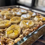 ['Close-up of a baked oatmeal dish topped with banana slices.', 'Side view of a warm banana baked oatmeal served in a bowl.', 'Deliciously baked oatmeal with an appealing golden-brown top and banana pieces.', 'Creamy banana baked oatmeal highlighted by a sprinkle of cinnamon.']