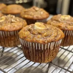 ['Close-up view of a moist Banana Chai Muffin showcasing its golden-brown top and specks of walnuts.', 'Side view of a delicious Banana Chai Muffin with a soft texture and visible chai spices.', 'Juicy Banana Chai Muffin displayed on a plate, highlighting its crumbly texture and banana pieces.', 'A freshly baked Banana Chai Muffin with a shiny, inviting crust and a sprinkle of walnut topping.']