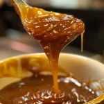 ['Close-up view of rich, golden-brown Bourbon Caramel Sauce in a glass jar.', 'Thick, luscious Bourbon Caramel Sauce swirling in a metallic saucepan.', 'Side view of homemade Bourbon Caramel Sauce glistening under soft light.', 'Spoon dripping with sweet Bourbon Caramel Sauce against a rustic background.']