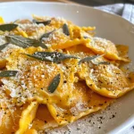 ['Close-up of Butternut Squash Ravioli drizzled with brown butter sage sauce.', 'Side view of golden Butternut Squash Ravioli topped with crispy sage leaves.', 'Juicy Butternut Squash Ravioli on a plate, garnished with brown butter and fresh sage.', 'Delicious Butternut Squash Ravioli showcasing a rich brown butter glaze and sage.']