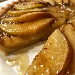 ['Close-up view of a caramelized upside-down pear tart with glistening pears and a golden crust.', 'Side view of a pear tart featuring succulent caramelized pears and a flaky pastry base.', 'Detailed shot of a delicious upside-down pear tart showcasing its glossy caramel layer and pear halves.', 'Appetizing image of a pear tarte tatin, highlighting the rich caramelization and baked texture.']