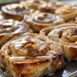 ['Close-up view of soft-baked apple cinnamon rolls topped with cream cheese frosting.', 'Side view of freshly baked apple cinnamon rolls, drizzled with icing and garnished with pecans.', 'Juicy, golden-brown apple cinnamon rolls displayed on a plate, showcasing their fluffy texture.', 'Warm, soft apple cinnamon rolls filled with diced apples, cinnamon, and sugar.']