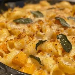 ['Close-up view of creamy butternut squash mac and cheese with a golden crust.', 'Side view of a serving of butternut squash mac and cheese, showcasing its creamy texture.', 'A vibrant dish of butternut squash mac and cheese, highlighting the pasta and cheese blend.', 'Rich, creamy butternut squash mac and cheese displayed in a bowl, garnished with herbs.']
