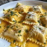 ['Close-up of creamy pumpkin ravioli with a buttery sauce and herbs.', 'Side view of freshly cooked pumpkin ravioli garnished with nuts and cheese.', 'Delicious plate of creamy pumpkin ravioli showcasing the rich sauce and herbs.', 'Juicy pumpkin ravioli served with a creamy white sauce and herbs.']