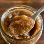 ['Close-up view of healthy apple butter in a jar with a spoon beside it.', 'Creamy apple butter spread on a slice of toast, surrounded by fresh apples.', 'A side view of a bowl of smooth apple butter, showcasing its rich texture.', 'Homemade apple butter in a glass jar with warm spices scattered around it.']