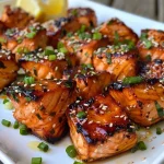 ['Close-up view of juicy Honey Garlic Salmon Bites garnished with sesame seeds and scallions.', 'Side view of succulent salmon cubes coated in honey garlic sauce, sprinkled with sesame seeds.', 'Delicious salmon bites in glaze, showing texture and garnishes of scallions and sesame seeds.', 'Appetizing close-up of golden-brown salmon pieces with a shiny honey garlic glaze, topped with herbs.']