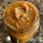 ['Close-up view of Keto Slow Cooker Pumpkin Butter in a jar.', 'Creamy Keto Pumpkin Butter in a bowl, with a spoon beside it.', 'Side view of Keto Pumpkin Butter spread on a slice of bread.', 'Textured pumpkin butter in a slow cooker, showing its rich, orange color.']