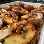 ['Close-up view of baked pears drizzled with maple syrup and sprinkled with cinnamon.', 'Side view of two juicy baked pears topped with nuts and a glossy syrup.', 'Delicious golden pears infused with cinnamon and maple syrup, garnished with pecans.', 'Warm, caramelized baked pears with a rich syrupy glaze and spices.']