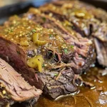 ['Close-up view of juicy Mississippi Pot Roast with a glossy sauce and vibrant pepperoncini.', 'Side view of a tender Mississippi Pot Roast, garnished with pepperoncini and melted butter.', 'Detailed image of Mississippi Pot Roast, showcasing its succulent texture and flavorful ingredients.', 'Close-up of Mississippi Pot Roast served with pepperoncini and drizzled with buttery sauce.']