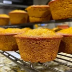 ['Close-up view of golden-brown pumpkin cornbread muffins on a wooden surface.', 'Side view of fluffy pumpkin cornbread muffins, showcasing their textured tops.', 'Juicy pumpkin cornbread muffins displayed on a rustic plate with warm lighting.', 'Freshly baked pumpkin cornbread muffins with a soft, moist interior, arranged beautifully.']
