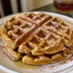 ['Close-up view of golden-brown pumpkin-spiced waffles stacked on a plate.', 'Side view of fluffy pumpkin waffles drizzled with syrup and topped with a dollop of whipped cream.', 'A serving of pumpkin-spiced waffles garnished with cinnamon and served on a rustic plate.', 'Delicious pumpkin waffles with a rich color, displayed with fall-themed decor.']