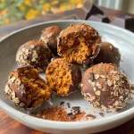 ['A close-up view of delicious pumpkin truffles coated in dark chocolate.', 'Side view of luscious pumpkin truffles with a smooth chocolate exterior and hints of pumpkin.', 'Close-up of gourmet pumpkin truffles highlighted by their rich chocolate glaze.', 'A delectable arrangement of pumpkin truffles showcasing a glossy dark chocolate coating.']