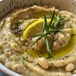 ['Close-up view of creamy Rosemary White Bean Dip in a bowl, garnished with fresh rosemary.', 'Side profile of a delicious white bean dip made with rosemary, garlic, and olive oil.', 'Appetizing Rosemary White Bean Dip displayed in a small dish, featuring a smooth texture and herbs.', 'Freshly made Rosemary White Bean Dip served with a drizzle of olive oil and a hint of garlic.']