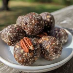 ['Close-up view of Turtle Energy Balls showcasing a rich, textured surface.', 'Side view of a Turtle Energy Ball with visible chocolate and nut layers.', 'Juicy Turtle Energy Balls displayed on a white plate, highlighting their glossy finish.', 'Detailed shot of a Turtle Energy Ball, emphasizing the medjool dates and nuts inside.']