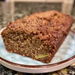 ['A close-up side view of a slice of apple cinnamon zucchini bread, showcasing its moist texture and apple chunks.', 'A detailed side angle of freshly baked apple cinnamon zucchini bread with visible cinnamon speckles and green zucchini.', 'A slice of apple cinnamon zucchini bread on a plate, highlighting its fluffy interior and bits of apple and zucchini.', 'A side view of delicious apple cinnamon zucchini bread, revealing its crusty top and soft, spiced crumb.']