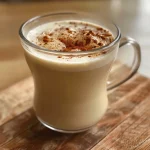 Close-up view of a creamy chai tea latte in a glass, garnished with ground cinnamon.