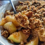Close-up view of a gluten-free apple crisp with oat crumble, showing golden-brown topping and juicy apples.