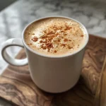 A close-up side view of a creamy pumpkin spice latte topped with foam and spices.