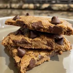 A close-up side view of a stack of gluten-free protein chocolate chip cookies, showcasing their chewy texture and chocolate morsels.